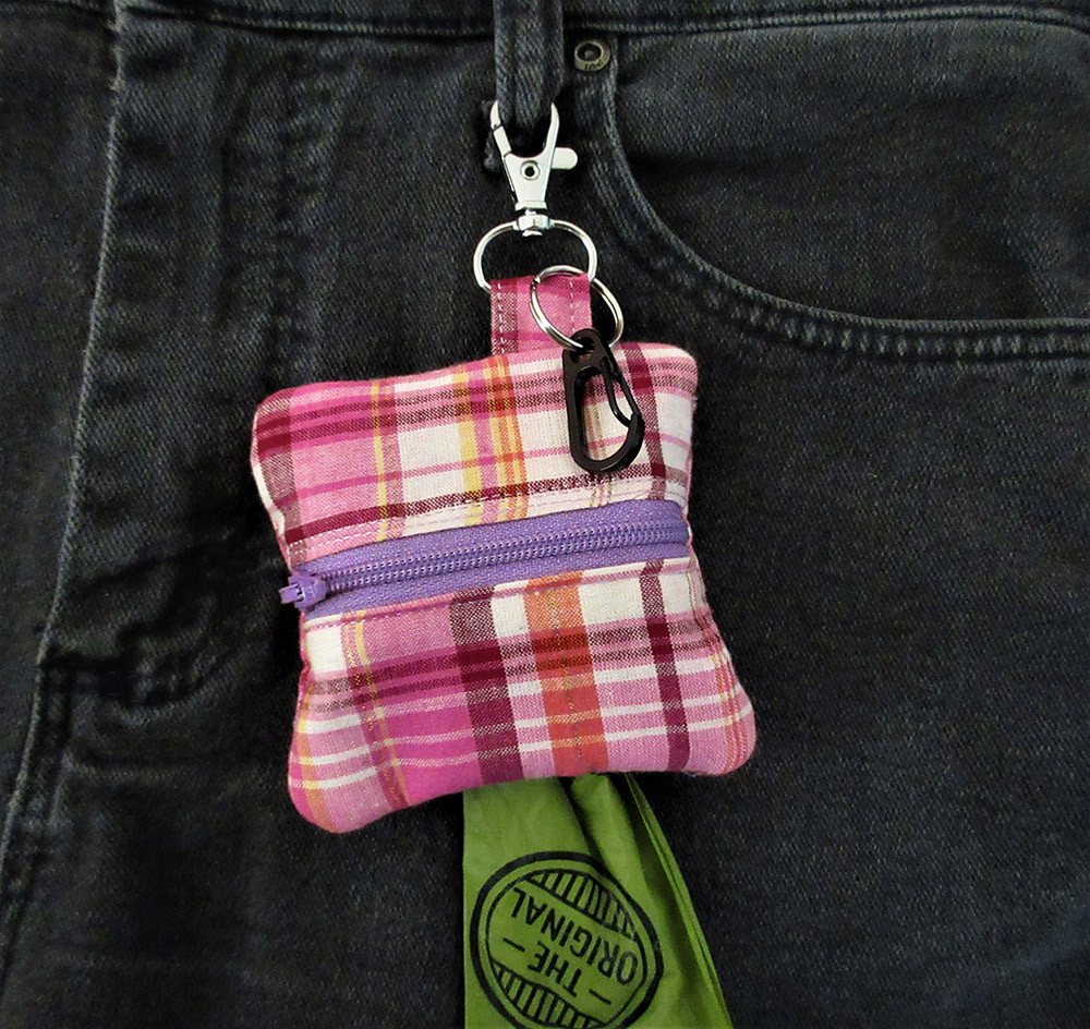 pink plaid poop bag holder or treat bag . 4 x 4 inches and comes with a free roll of bags.  Zipper Close and clip to hold used bags.